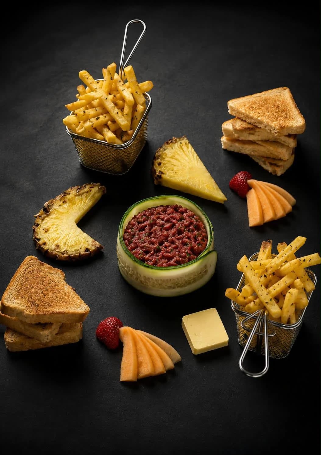 Rindstartare in einem Gurkenring, auf Schieferplatte serviert mit Pommes frites, Toast und Ananas