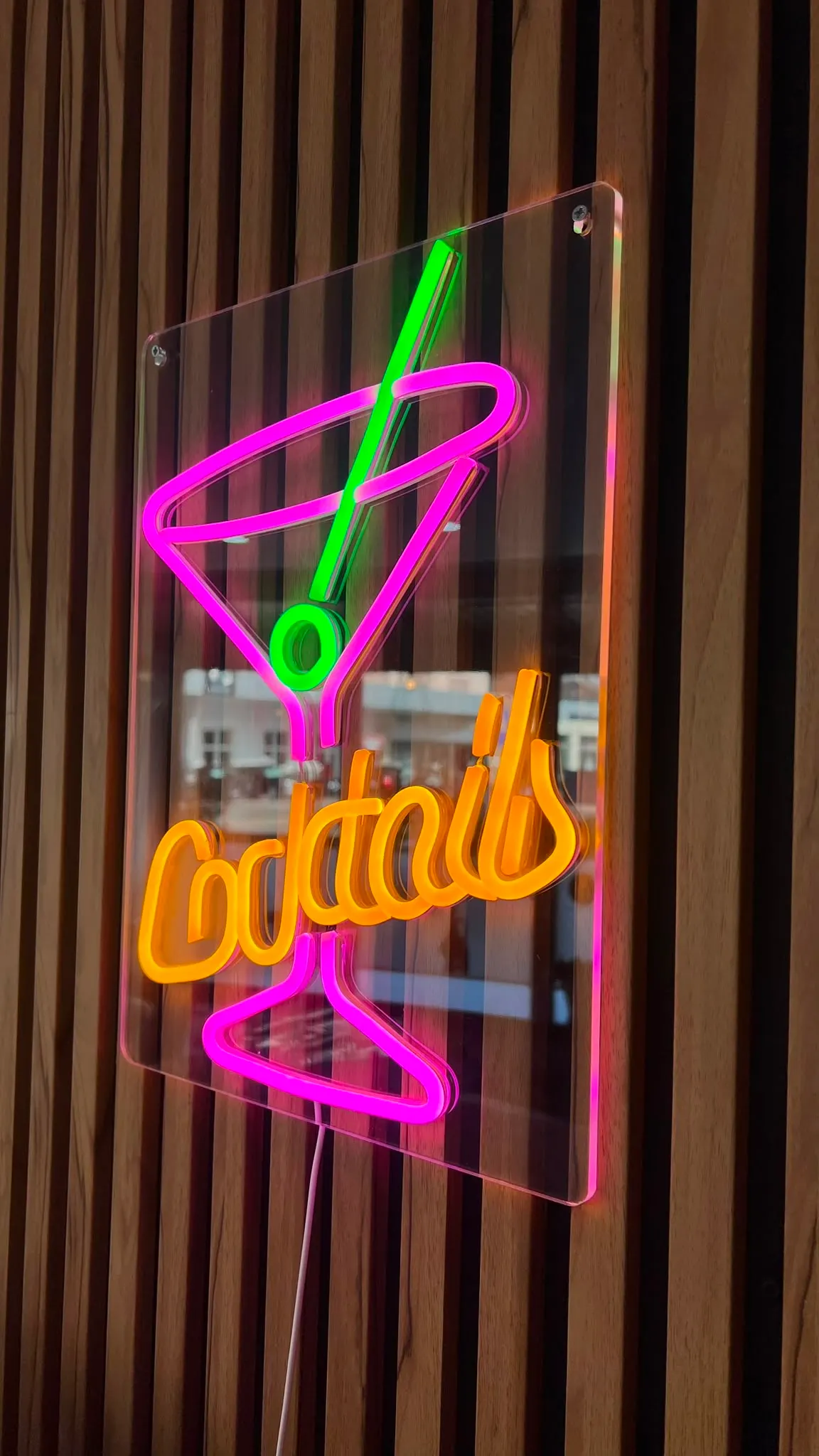 The pink and orange “Cocktails” neon sign on the slatted wall