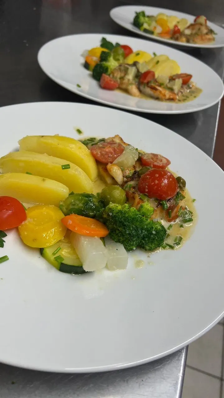 A pan-fried fish fillet, potatoes, tomatoes and broccoli, sauce on the side